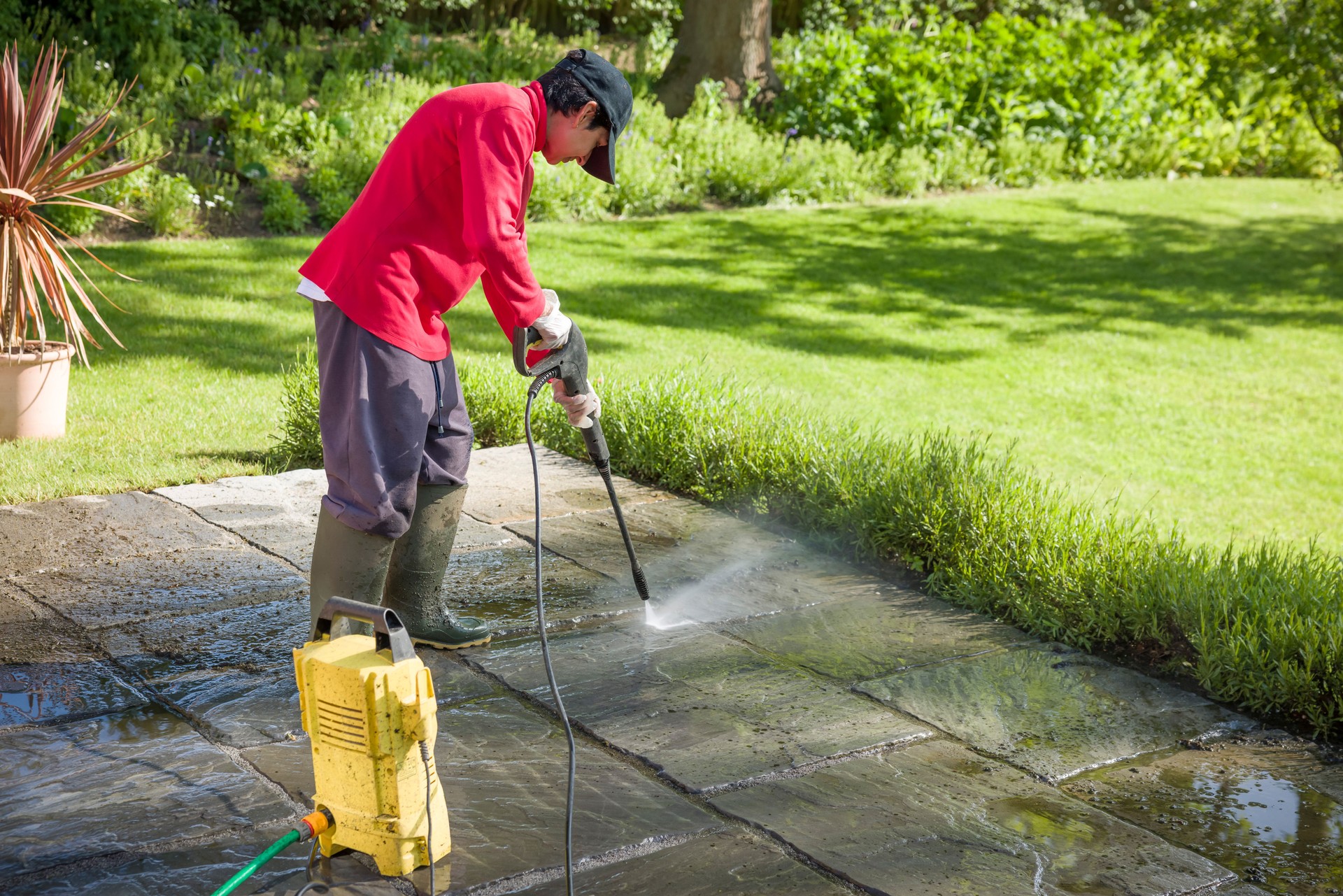 Jet washing, woman high pressure washing a garden patio, UK
